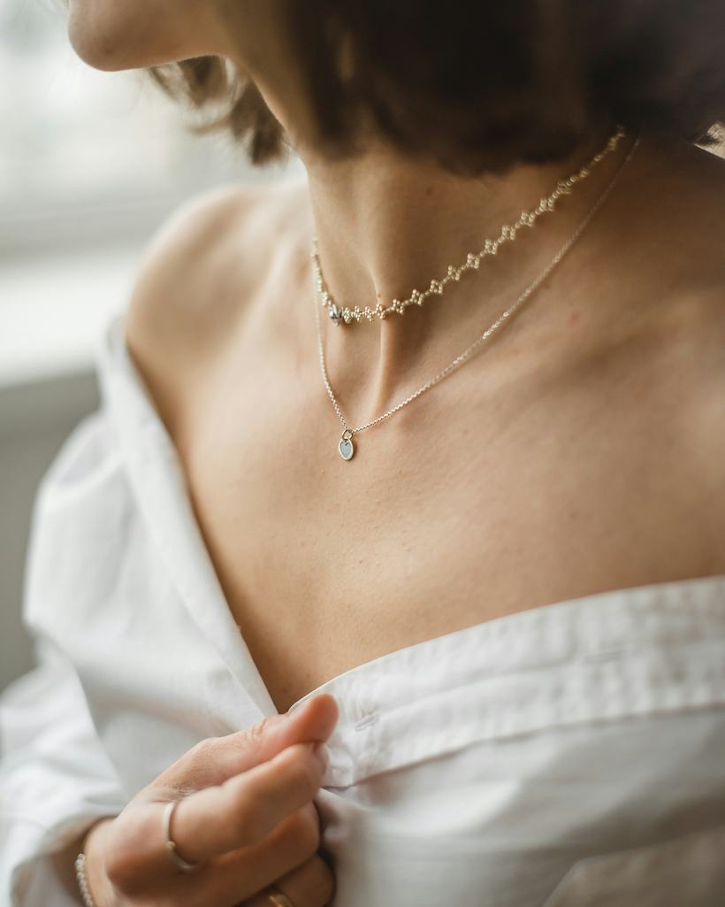 The Meera necklace worn at the collarbone — a fine gold-plated chain with a single shell-pearl drop